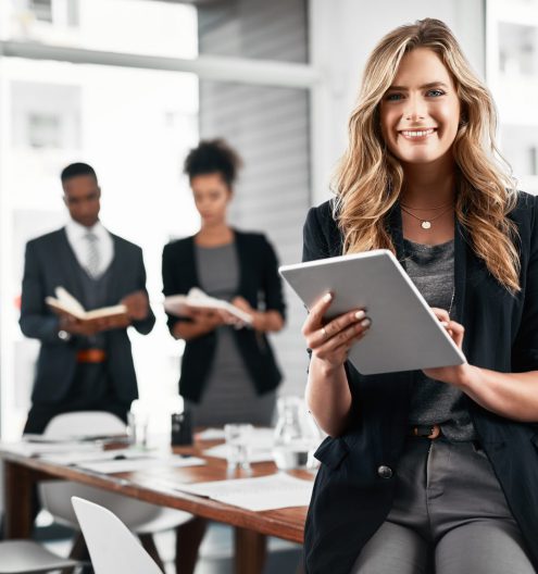 Portrait of a young businesswoman using a digital tablet in an office with her colleagues in the background.